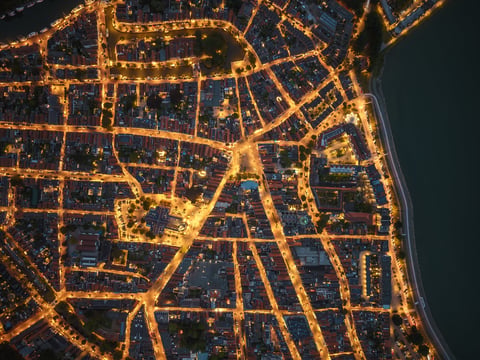 Drone aerial perspective of historic waterfront town at night with illuminated streets