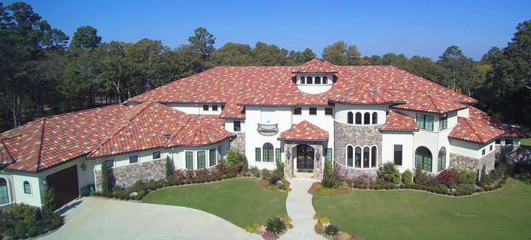 Large white Mediterranean-style mansion with red tile roof, multiple arches and domed sections, surrounded by manicured lawn and trees