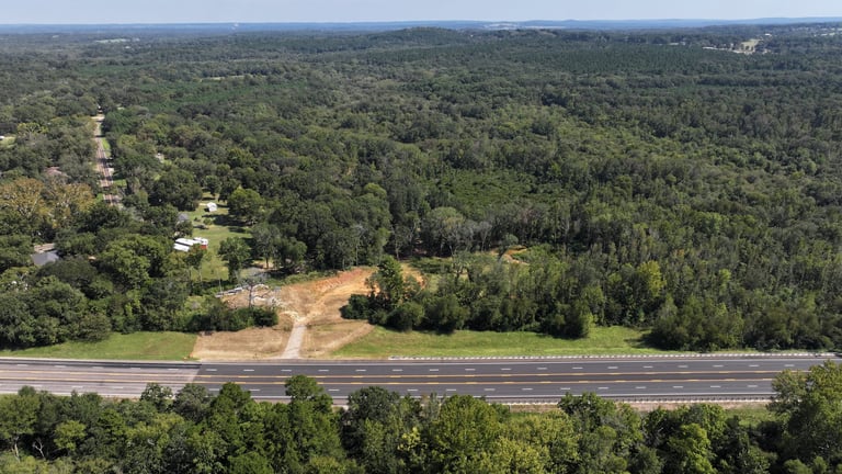 Aerial view of a multi-lane highway cutting through dense forest with cleared land and scattered houses visible
