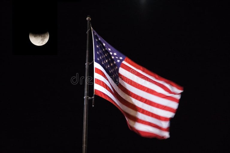 American flag waving on a flagpole at night with the moon visible in the background against a dark sky