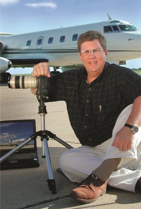 Man holding telephoto lens with camera on tripod near commercial aircraft on tarmac