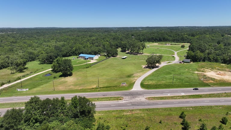 Aerial view of a rural property with green pastures, a home with blue pool, and curved driveway bordered by trees