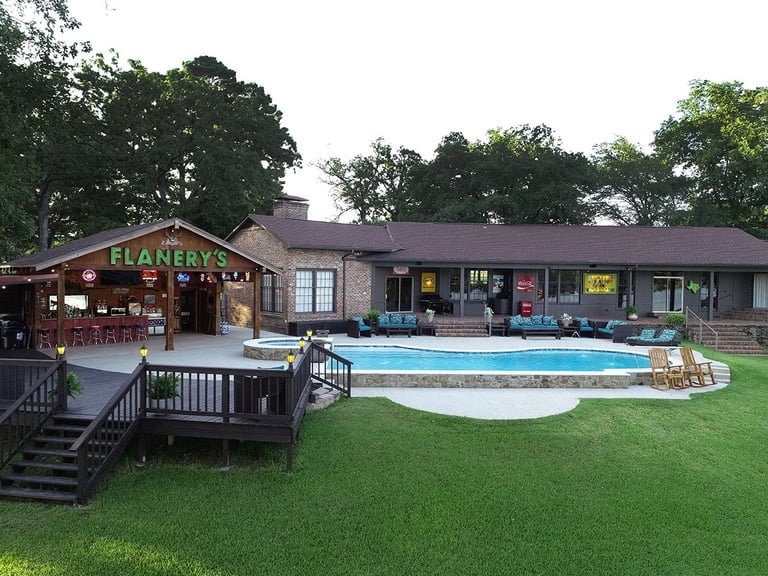 Brick residential building with swimming pool in backyard, wooden deck, and Flanerys storefront on the left side with manicured lawn