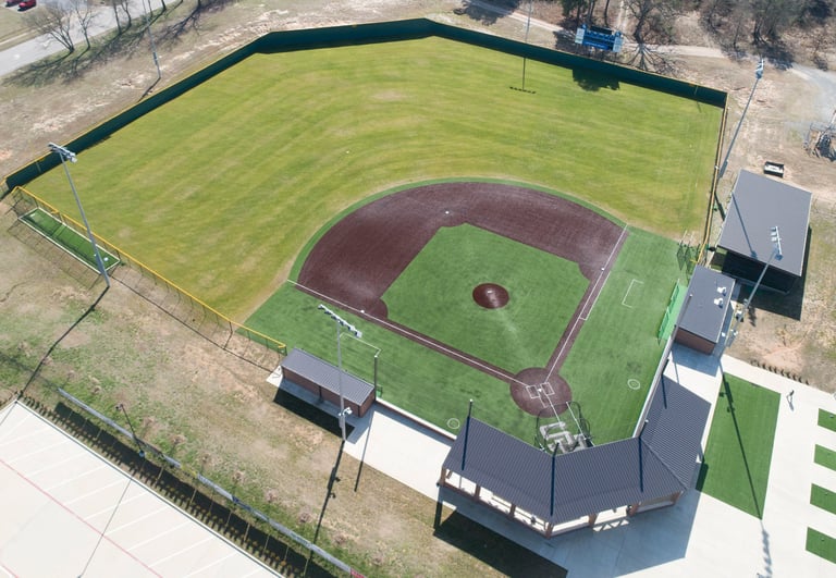 Aerial view of a baseball field with brown infield, green outfield, and dugout structures on the sides