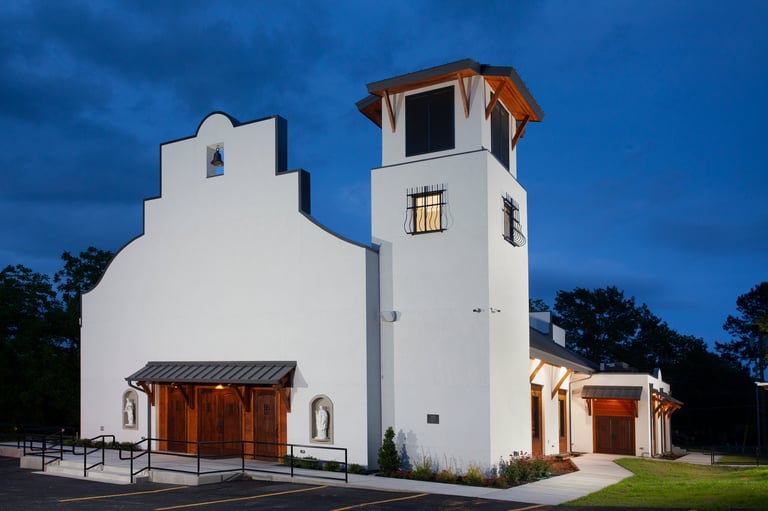 White modern church building with tall bell tower against blue twilight sky and green grass