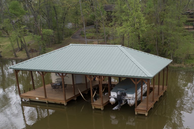 Elevated boathouse with metal roof and wooden wraparound deck surrounded by water and trees