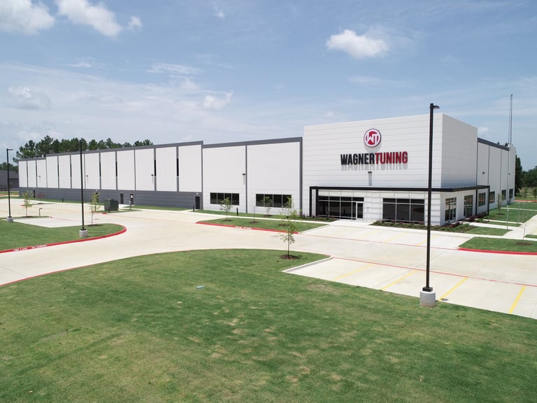Modern Warner Tuning industrial building with white exterior, metal panels, and landscaped grounds under blue sky