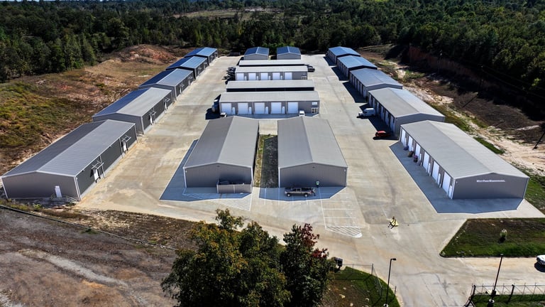 Aerial view of an industrial facility with multiple metal buildings arranged around a central courtyard surrounded by forest