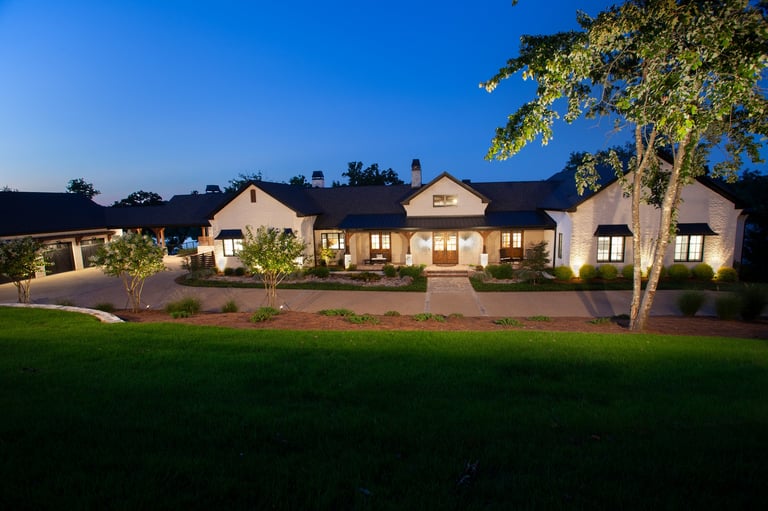 Illuminated modern ranch-style home with manicured lawn and landscaping at dusk