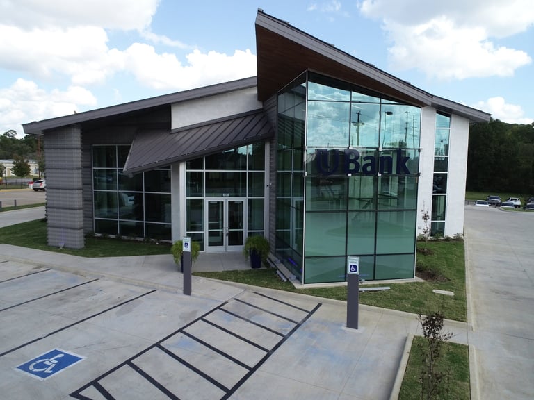 Modern commercial building with glass corner entrance, flat roof, and accessible parking spaces on concrete lot.