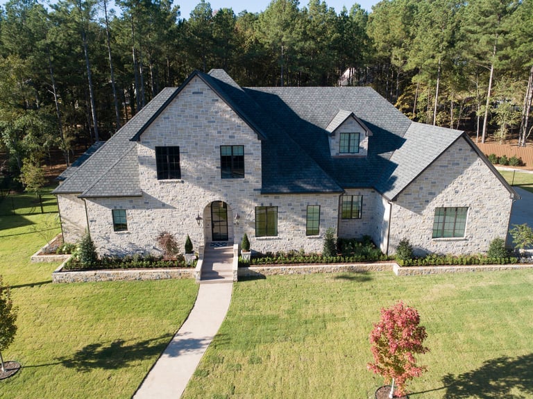 Modern two-story white brick home with gray roof and manicured lawn surrounded by pine trees