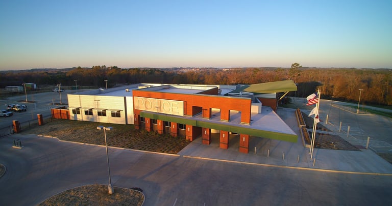 Aerial view of a modern two-story industrial building with orange and yellow exterior walls at dusk, surrounded by parking area and bare trees