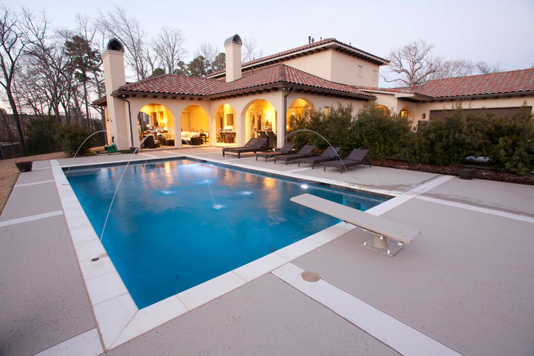 Luxurious home with illuminated interior, spacious patio, and rectangular swimming pool at dusk