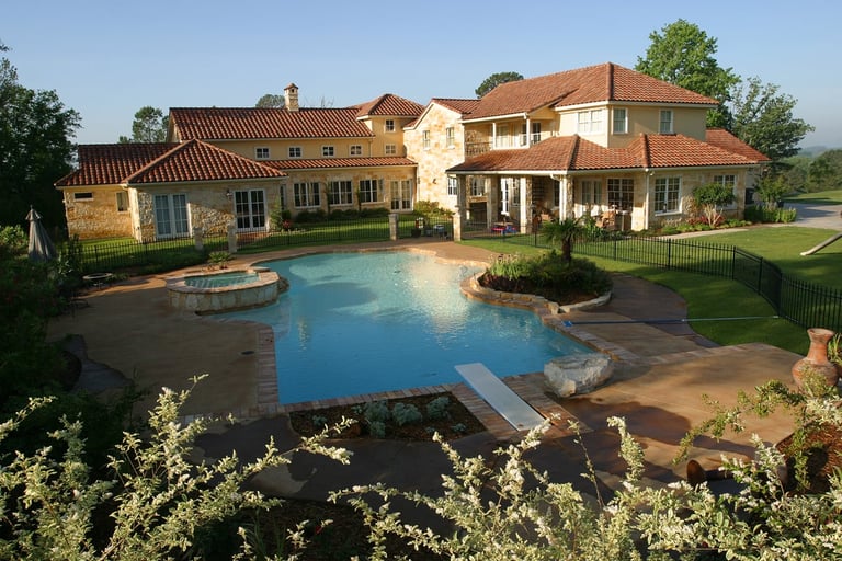 Luxury mansion with terracotta roof overlooking a large blue swimming pool and manicured landscaping on expansive grounds