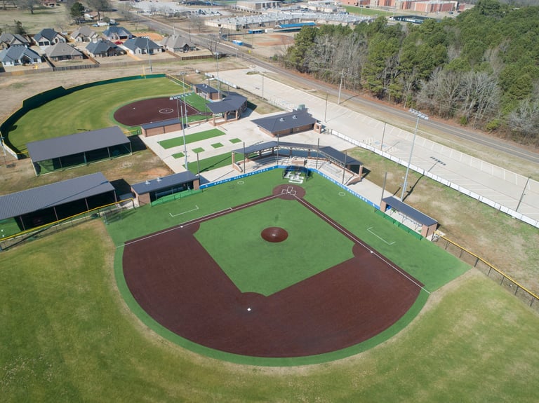 Aerial view of a baseball complex with multiple fields, dugouts, and a residential area in the background