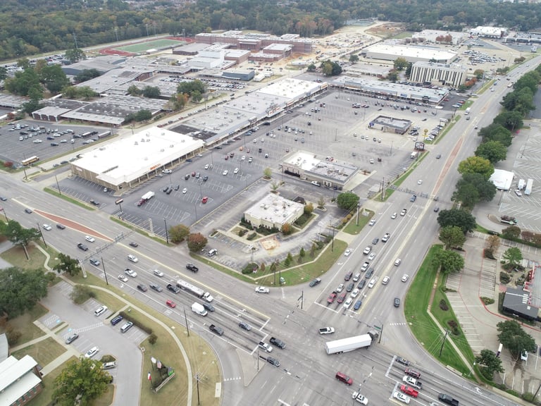 Aerial view of large retail shopping center with expansive parking lots and surrounding commercial buildings
