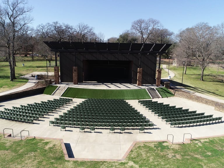 Outdoor amphitheater with green seating and a black stage structure surrounded by bare trees in a park setting