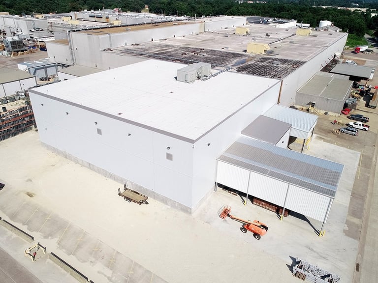 Aerial view of large commercial building under construction with white roof, surrounding industrial area, and construction equipment
