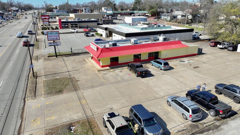 Aerial view of a red and yellow commercial building with parking lot and parked vehicles in a suburban strip mall area