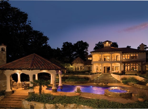 Luxurious mansion at dusk with illuminated pool, gazebo, and manicured landscaping