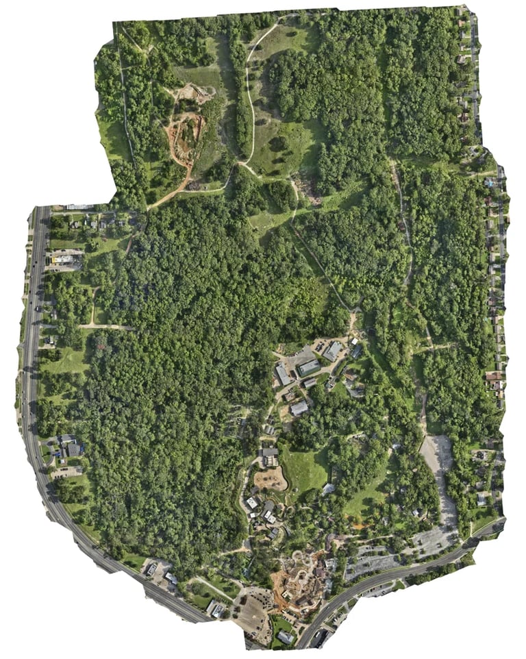 Aerial view of a large forested park with winding paths, buildings, and clearings surrounded by dense green trees