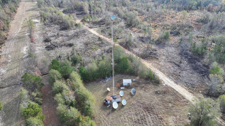 Aerial view of harvesting equipment and workers in a forested area with cleared sections and dirt roads