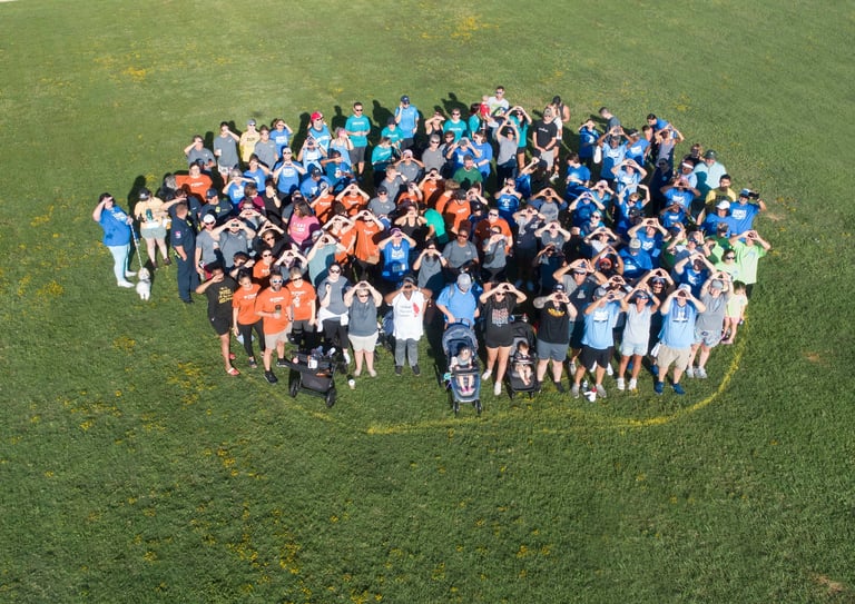 Large group of people gathered in a circle on a grassy field, viewed from above.