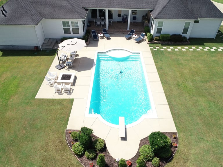 Aerial view of a backyard with a turquoise swimming pool, patio furniture, and a house with attached structures.