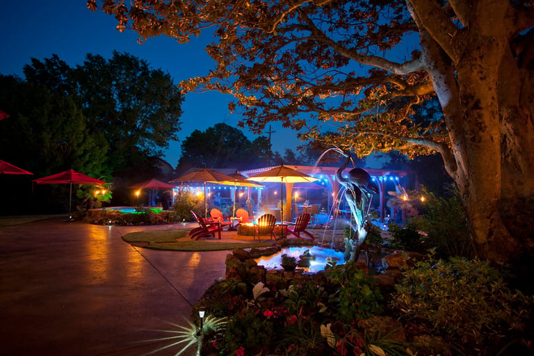 Illuminated vintage airstream trailer at night surrounded by garden landscaping and trees with blue evening sky
