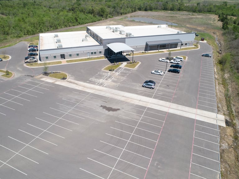Aerial view of a large commercial building with parking lot surrounded by wooded area