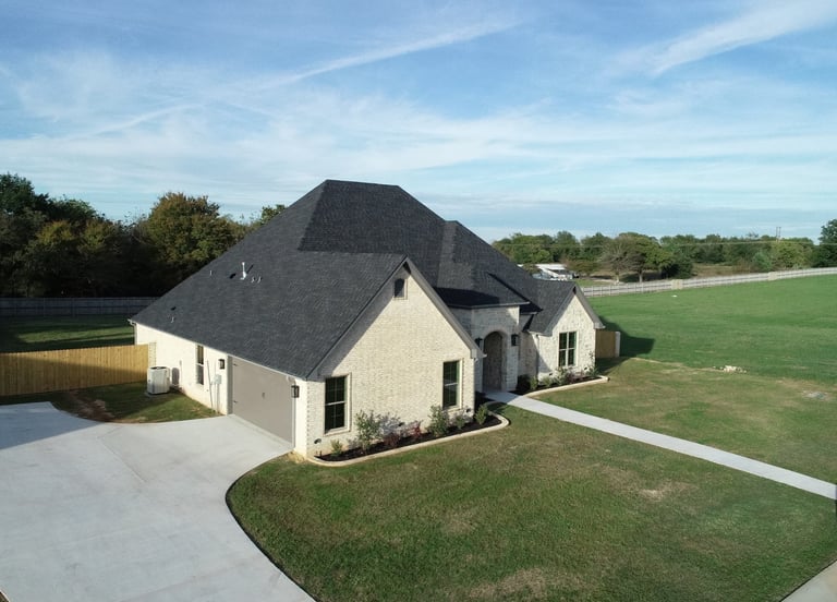 Aerial view of a modern white brick residential home with dark roof on a large suburban lot