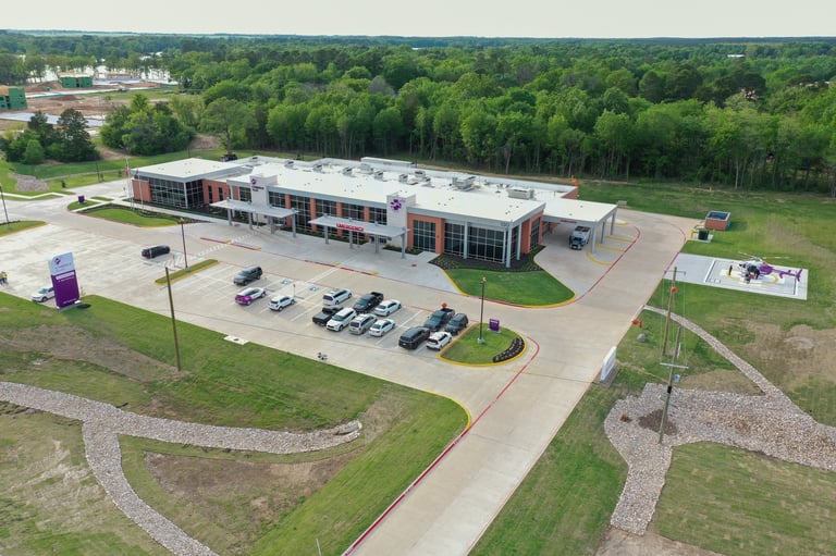 Aerial view of a modern commercial building with parking lot surrounded by green trees and landscaped grounds
