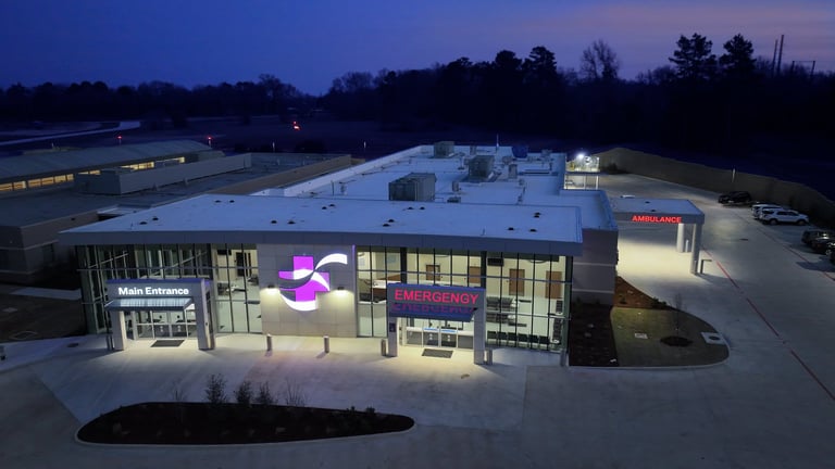 Modern commercial building with illuminated purple logo at dusk, featuring glass storefront and white flat roof in parking lot setting