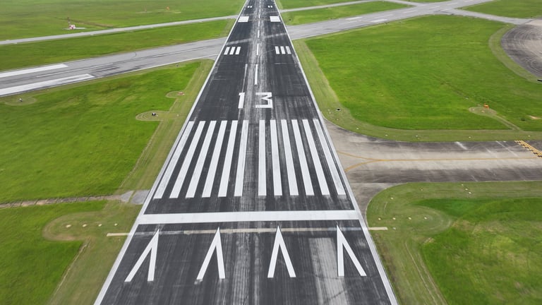 Aerial view of airport runway with white striped markings and directional arrows on asphalt surrounded by green grass
