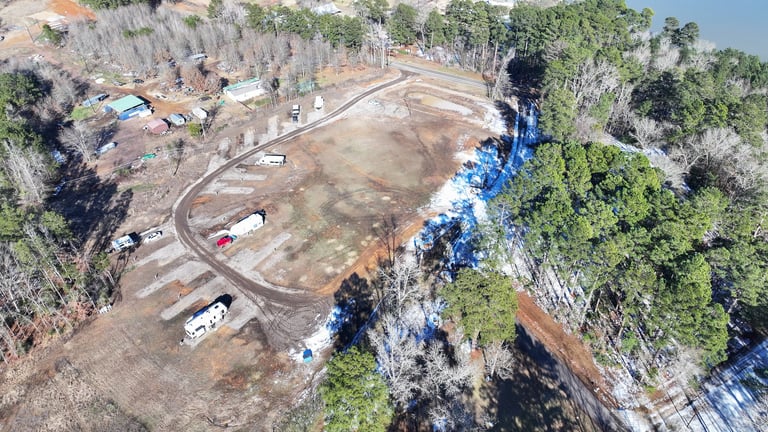 Aerial view of a cleared construction site surrounded by trees and forest with equipment and vehicles on brown dirt ground