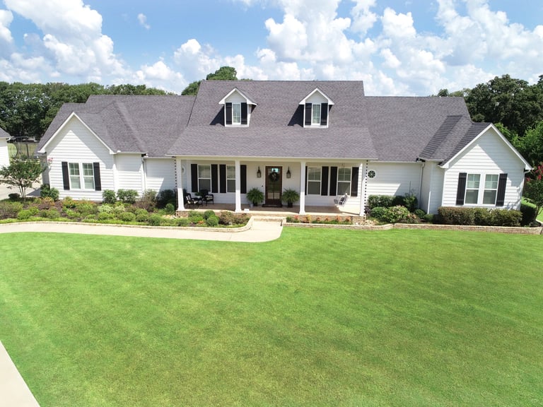 White single-story house with gray roof, front porch, and dormer windows on manicured green lawn.