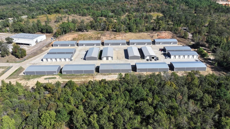 Aerial view of large modern warehouse facility with solar panels on roof surrounded by forested area